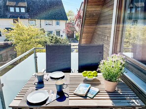 A balcony with a table set for two, a bowl of green apples, a potted plant, and a book. - Land in Sicht by Interhome (Mengen)