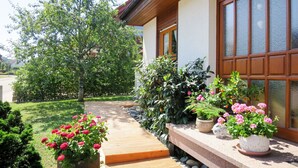 Een huis met een houten terras, plantenbakken en een pad van stenen.