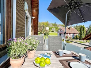 An outdoor patio with a table set for dining, potted plants, and a view of a traditional house in the background. - Land in Sicht by Interhome (Mengen)