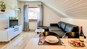 Een moderne woonkamer met een televisie, bank, eettafel en een fles wijn.