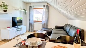 Een moderne woonkamer met een televisie, bank, eettafel met wijnglazen en een fles wijn.