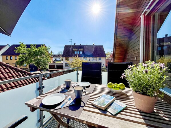 A balcony with a table set for two, a potted plant, and a view of houses in the background. - Land in Sicht by Interhome (Mengen)