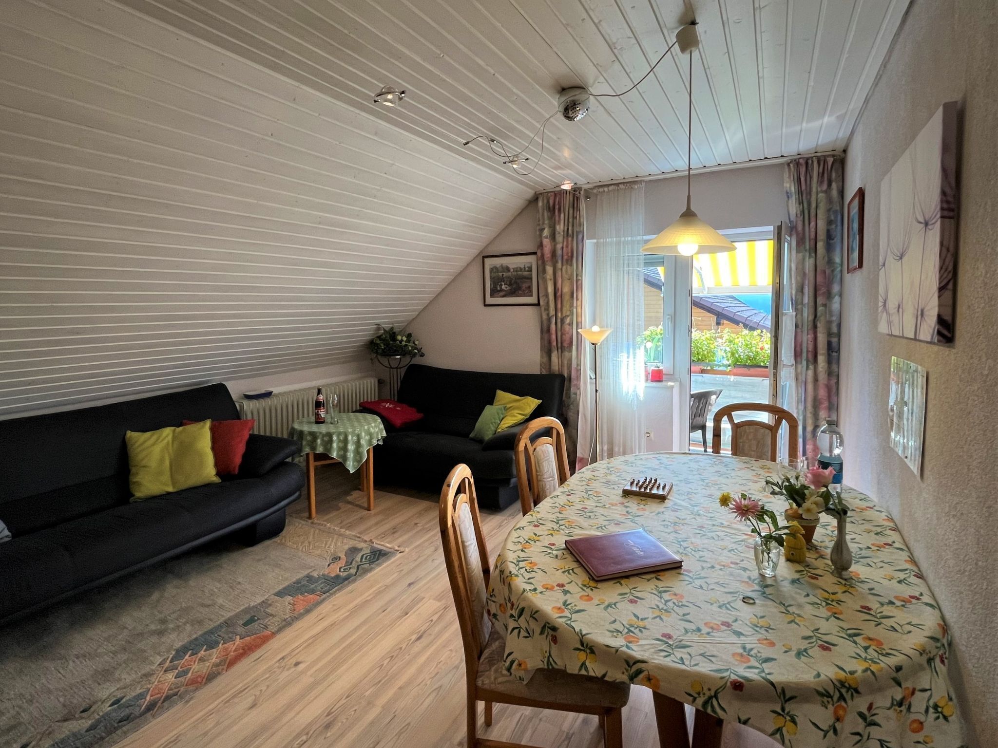 A cozy living room with a black sofa, a small table with a green tablecloth, and a dining table with a floral tablecloth.