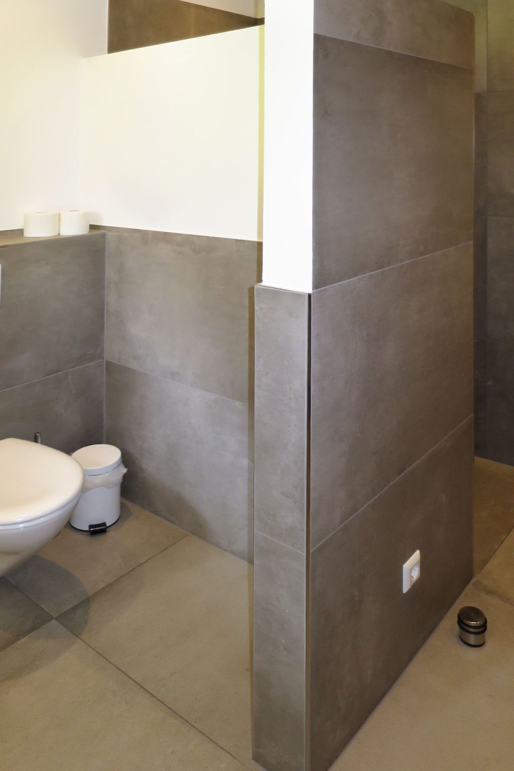 A bathroom with a toilet, a trash bin, and a towel dispenser.