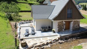 A house with a sloped roof, stone walls, and a patio with outdoor furniture.