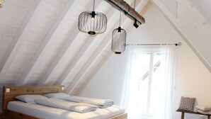 A loft bedroom with a wooden bed, two hanging light fixtures, and a view of the outdoors.