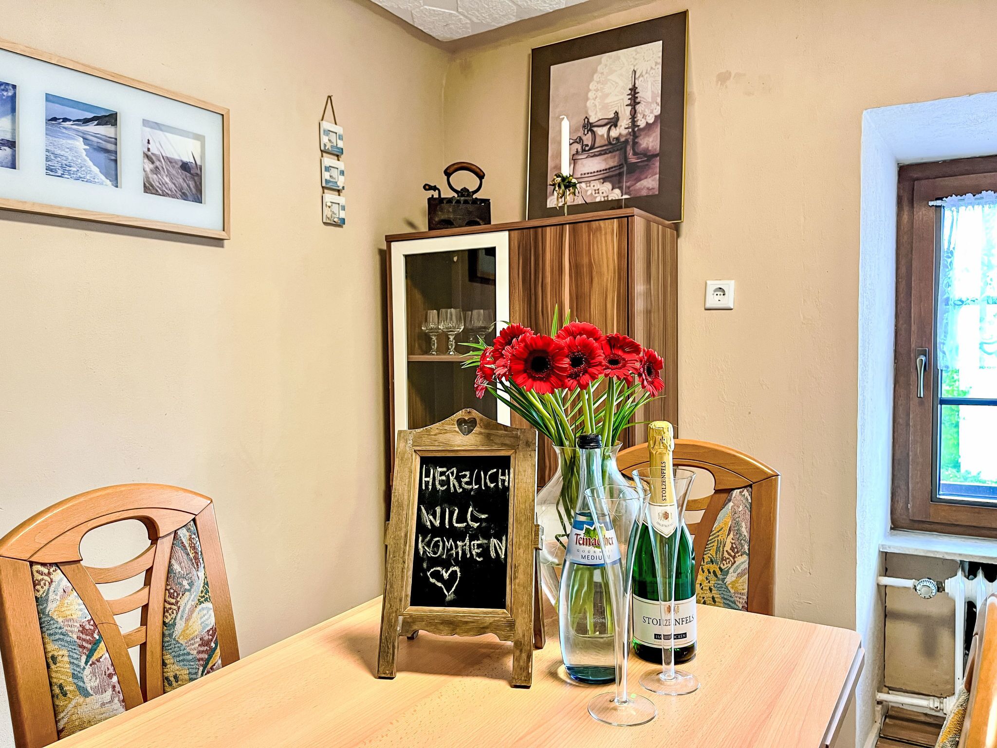 Een eettafel met een krijtbord, een vaas rode bloemen en twee flessen wijn.