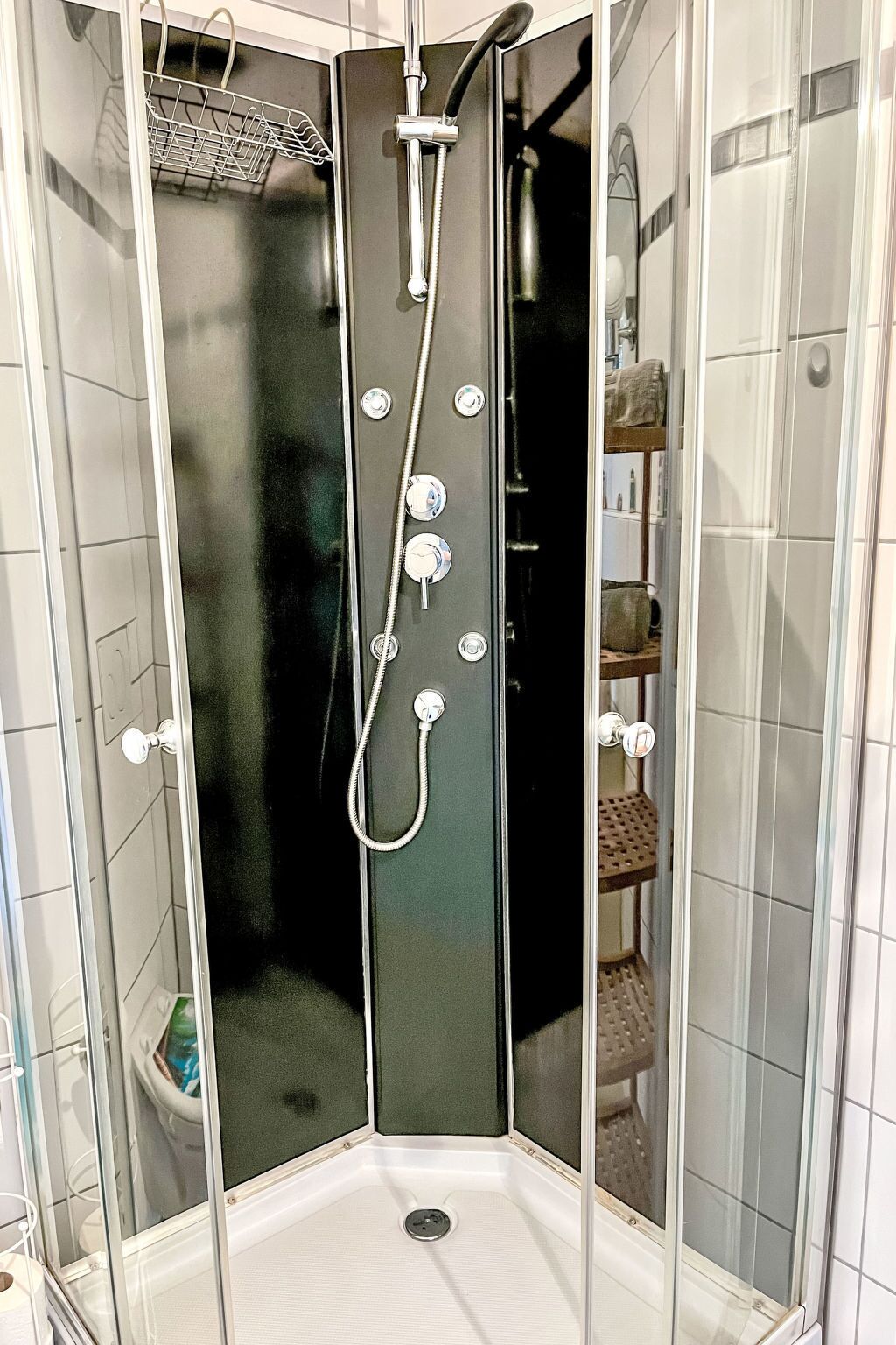En dusch i ett hörn med en vägg av glas, flera kranar och ett duschmunstycke som kan hållas i handen.