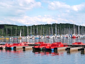 A marina with numerous sailboats docked, surrounded by a forested hillside.