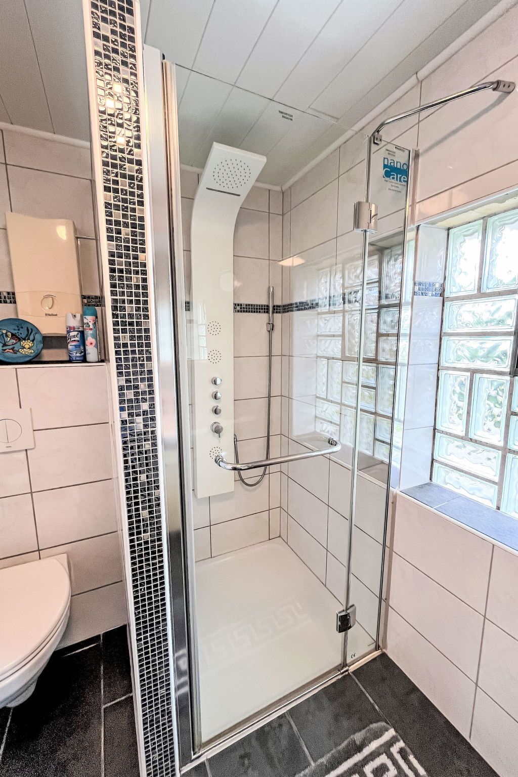 Un baño moderno con cabina de ducha de vidrio, inodoro y ventana con azulejos decorativos.