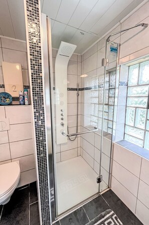A modern bathroom with a glass shower enclosure, a toilet, and a window with decorative tiles. - Holiday-Home Nr 1 am Bostalsee by Interhome (Oberthal)