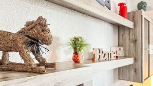 Een rustiek houten plankje met een strooien sculptuur van een paard, een kleine potplant en decoratieve items, waaronder een bordje met de tekst 'Home'.