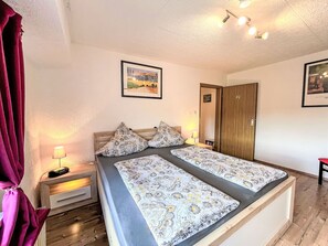 A double bed with patterned bedding, a nightstand with a lamp, a wooden wardrobe, and two framed pictures on the walls. - Holiday-Home Nr 1 am Bostalsee by Interhome (Oberthal)