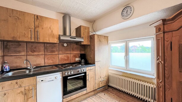 Eine Küche mit Holzschränken, einem Herd, einem Backofen, einem Geschirrspüler und einem Fenster mit Blick auf Grünflächen.