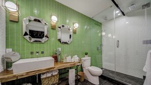 Un bany modern amb una paret de rajoles verdes, un moble de bany de fusta, un lavabo blanc, una tassa i un espai de dutxa amb envidriament.