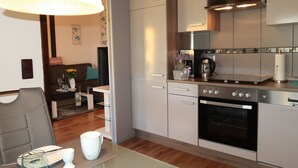 A modern kitchen with stainless steel appliances, a dining area with a glass table, and a cozy living space with a sofa and decorative pillows.