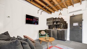 A modern living room with a grey sofa, a small round table, and a kitchen area with a hexagonal backsplash.
