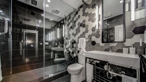 A modern bathroom with a glass-enclosed shower, a white toilet, and a sink with a mirror above it.