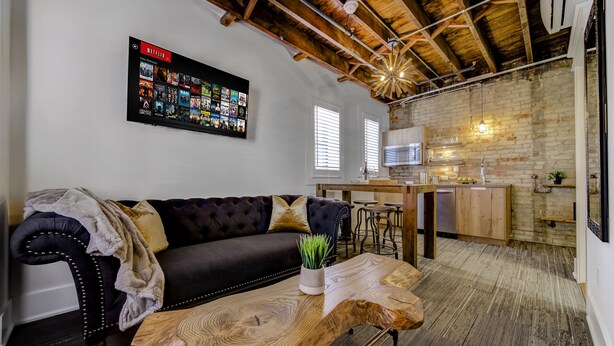 A living room with a dark leather sofa, a wooden coffee table, and a mounted Netflix screen. - Westlake Hotel - The Noire Suite (Etobicoke)