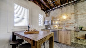 A kitchen with a wooden table, bar stools, a microwave, and a brick wall. - Westlake Hotel - The Noire Suite (Etobicoke)
