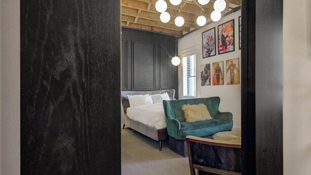 A bedroom with a bed, a green sofa, and a ceiling light fixture. - Westlake Hotel - The Art Suite (Etobicoke)