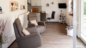 A modern living room with a sofa, chairs, a TV, and a kitchen in the background. - Vacation home Caro by Interhome (Kirburg)