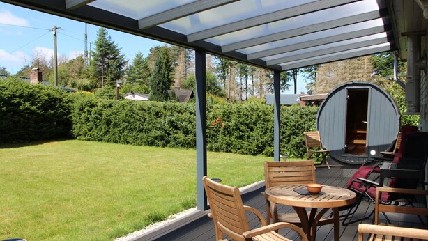A covered patio with wooden furniture, a round table, and a barrel. - Vacation home Caro by Interhome (Kirburg)