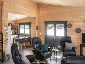 A cozy wooden cabin interior with a dining area, two leather sofas, a small table with candles, and a kitchen visible through an open door. - Ferienhaus Barbara by Interhome (Enspel)