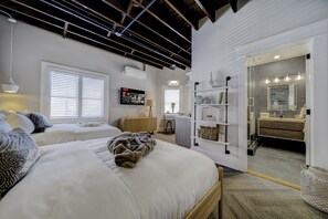 Une chambre moderne avec deux lits, un bureau et une salle de bain visible à travers une porte ouverte.