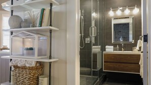 Une salle de bain moderne avec une douche à parois de verre, un meuble-lavabo en bois et une étagère murale sur laquelle sont disposés divers objets.