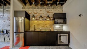 Une cuisine moderne avec des appareils en acier inoxydable, un mur en briques, des luminaires suspendus et une moquette rouge.