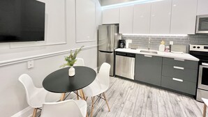 Una cocina moderna con armarios blancos, un refrigerador de acero inoxidable, un lavavajillas y un microondas. Hay una pequeña isla con un lavamanos y una planta en maceta.