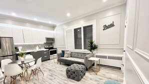 Una cocina moderna con armarios blancos, un sofá gris y un comedor con sillas blancas y una mesa pequeña.