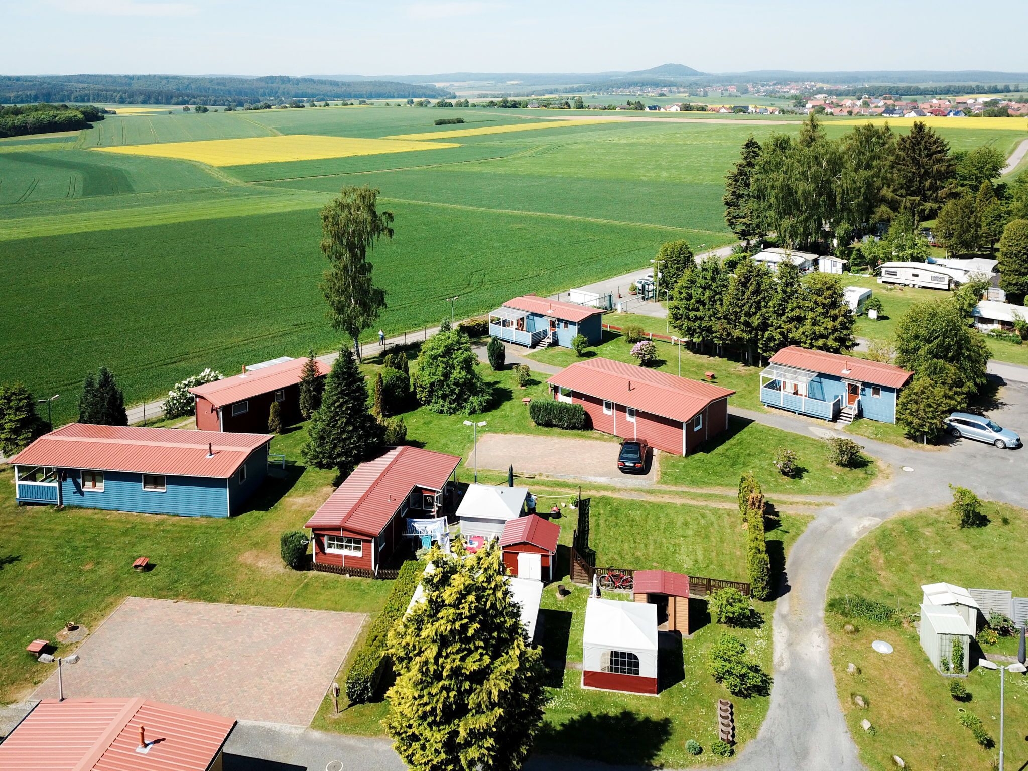 Eine Vogelperspektive eines ländlichen Campingplatzes mit mehreren Hütten, einem zentralen Gebäude und umliegenden Feldern.