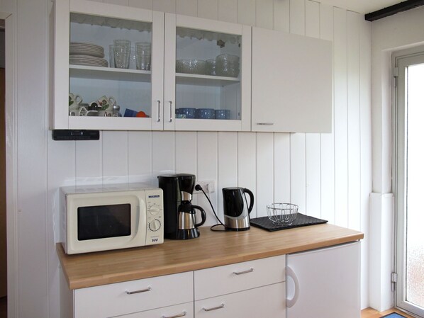 A kitchen with white cabinets, a microwave, a coffee maker, and a glass container on the countertop.