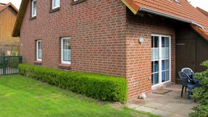 A two-story brick house with a sloped roof, a front door, and a small patio with chairs. - Kitowski by Interhome (Hooksiel)