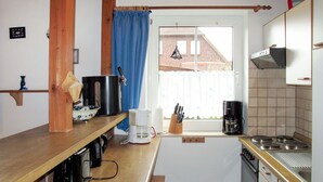 A compact kitchen with a wooden countertop, coffee maker, kettle, and a window with a view of a brick building. - Kitowski by Interhome (Hooksiel)