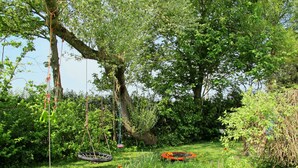 Ein üppiger Garten mit Schaukel, Trampolin und verschiedenen Pflanzen und Blumen.