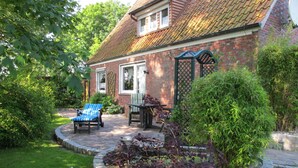 Ein Ziegelhaus mit Ziegeldach, ein Kiesweg, ein blauer Stuhl und ein Garten mit verschiedenen Pflanzen.