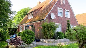 Ein rotes Ziegelhaus mit geneigtem Dach, einer Satellitenschüssel und einem Garten mit Rasenfläche und kleinem Teich.