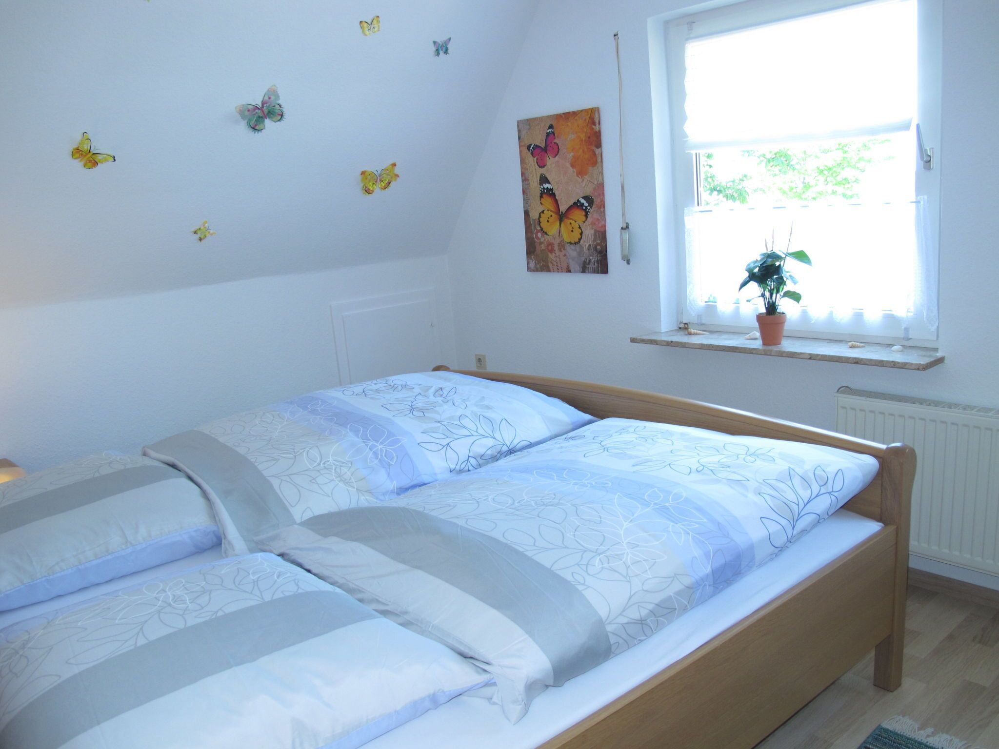 Quarto com cama, janela com planta e adesivos de borboletas na parede.