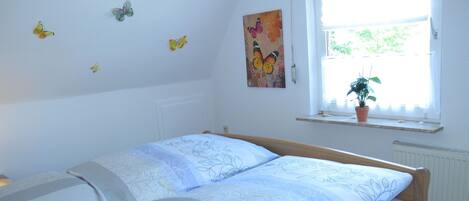 Quarto com cama, janela com planta e adesivos de borboletas na parede.