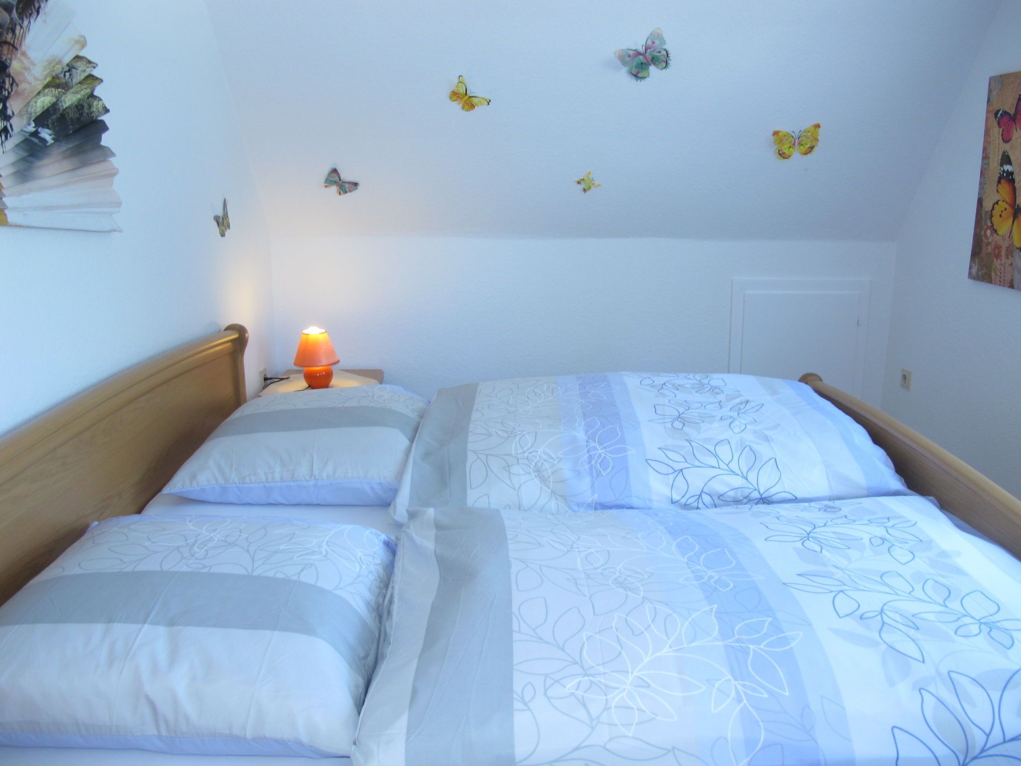 Une chambre à coucher avec un lit, des oreillers, une table de chevet avec une lampe et des autocollants décoratifs représentant des papillons sur le mur.