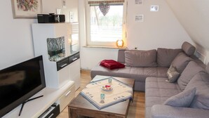 Ein kompakter Wohnbereich mit Fernseher, Couchtisch, Sofa und einer kleinen Küchenzeile.