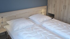 Ein ordentlich bezogenes Bett mit weißer Bettwäsche in einem Zimmer, das ein Holz-Kopfteil und ein heller Kleiderschrank aufweist.