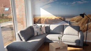 Ein modernes Wohnzimmer mit einer Eckcouch, einem Holztisch und einem großen Fenster mit Blick auf einen Strand.