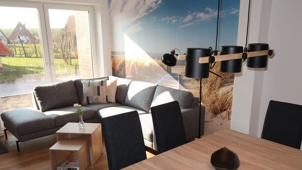 Ein modernes Wohnzimmer mit einem Ecksofa, einem Esstisch und Stühlen. Ein großes Fenster bietet Blick auf Häuser und einen Garten.