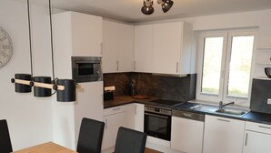 Eine moderne Küche mit weißen Schränken, einem eingebauten Ofen, einer Mikrowelle und einem Spülbecken. Ein Holztisch mit Stühlen steht bereit.