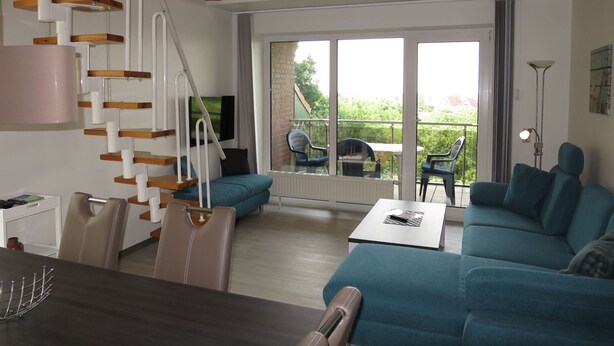 Una sala de estar moderna con una escalera, un comedor y un balcón con mobiliario exterior.