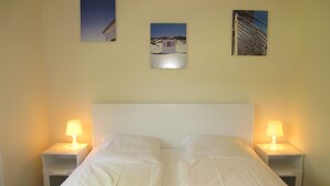 Una cama doble con dos mesitas de noche, cada una con una lámpara. Encima de la cama, hay tres cuadros enmarcados en la pared.